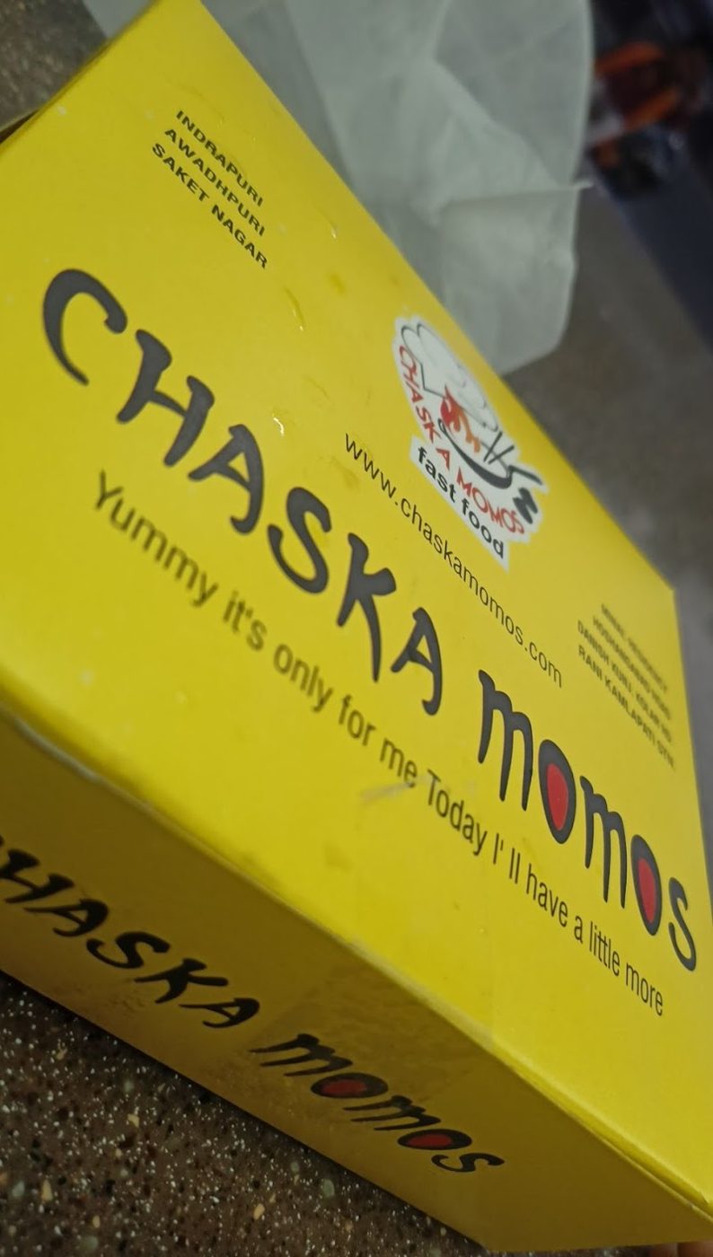 Chaska Momos yellow takeaway box with logo and tagline